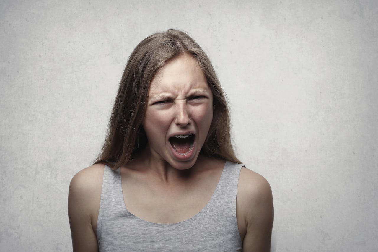 A woman with an intense facial expression screaming against a neutral gray background.