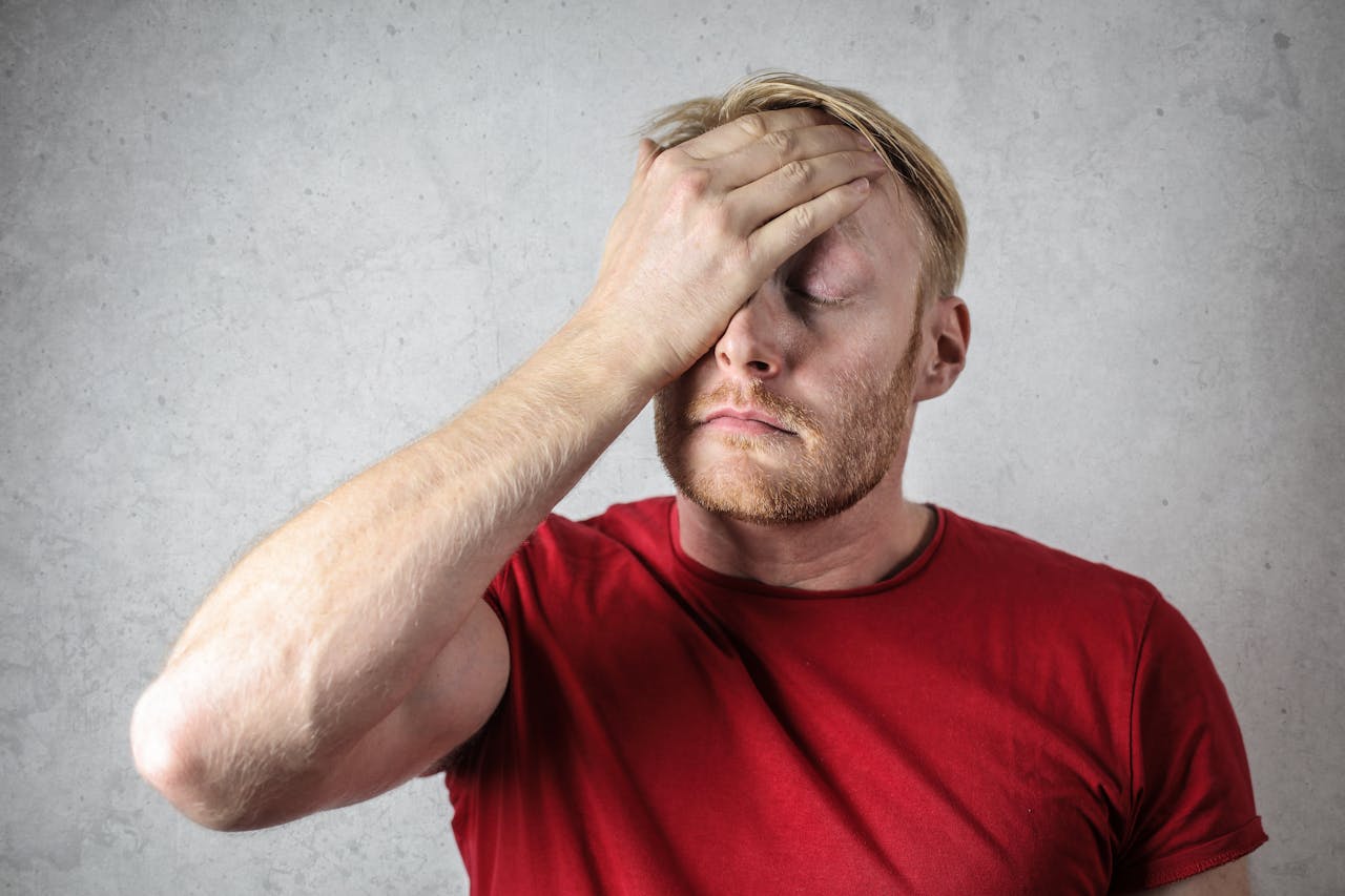 gallery-3 A frustrated man in a red shirt holds his head in stress against a neutral background.